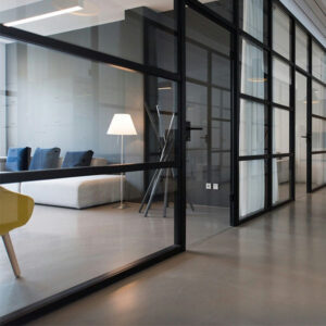 Modern office interior with glass partitions, gray sofa, and floor lamp.