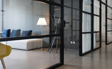 Modern office interior with glass partitions, gray sofa, and floor lamp.