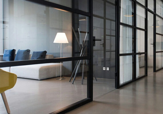 Modern office interior with glass partitions, gray sofa, and floor lamp.
