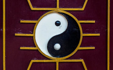 Yin and Yang symbol with golden geometric patterns on a maroon background.