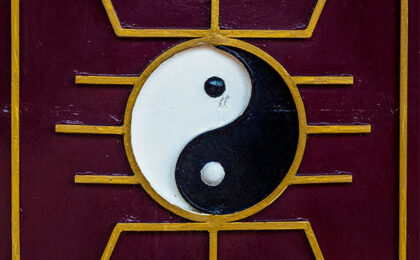 Yin and Yang symbol with golden geometric patterns on a maroon background.