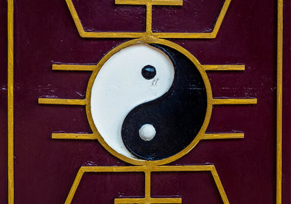 Yin and Yang symbol with golden geometric patterns on a maroon background.