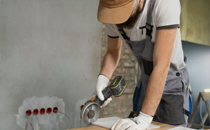 Construction worker using a power tool to cut material on a workbench during home renovation.