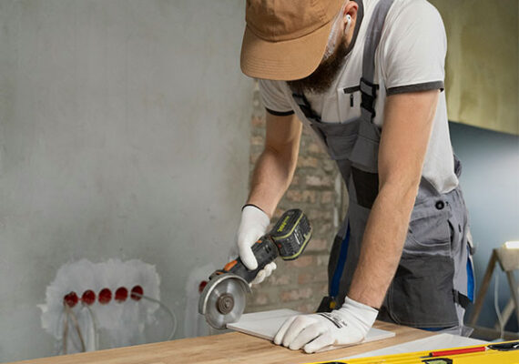 Construction worker using a power tool to cut material on a workbench during home renovation.