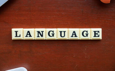Word “LANGUAGE” spelled out with letter tiles on a wooden table.