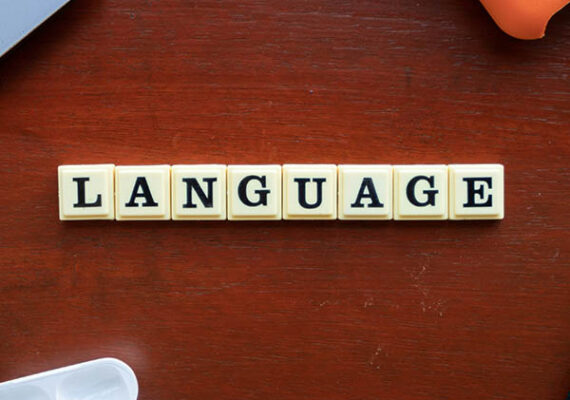 Word “LANGUAGE” spelled out with letter tiles on a wooden table.