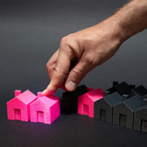 Hand placing a bright pink miniature house among a row of black model houses.