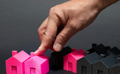 Hand placing a bright pink miniature house among a row of black model houses.