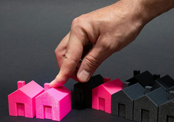 Hand placing a bright pink miniature house among a row of black model houses.